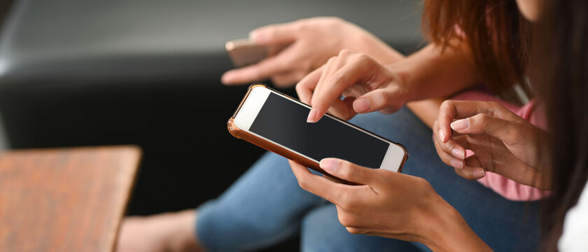 Cropped image of women is using a black blank screen smartphone while sitting in the living room.