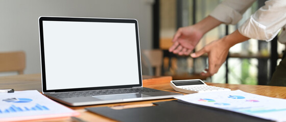 An empty screen computer laptop is putting on a wooden working desk surrounded by various equipment.