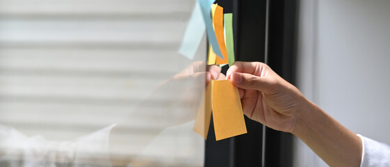 Cropped image a hand is holding an empty sticky note at the glass wall.