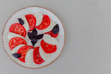 Caprese salad. Mozzarella cheese, tomatoes and basil herb leaves on plate. Top view with copy space