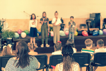 Children's holiday in elementary School. Children on stage perform in front of parents. image of blur kid 's show on stage at school , for background usage. Blurry. toned