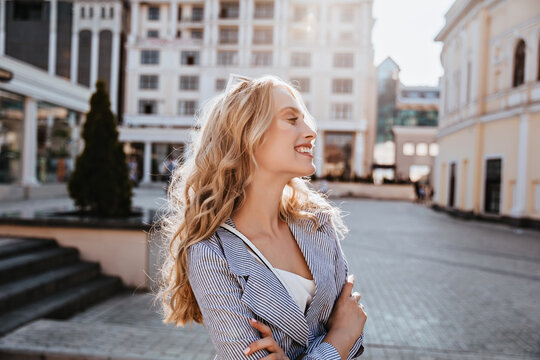 Glad white girl with blonde hair enjoying city view. Outdoor photo of pretty caucasian female model standing on the street.