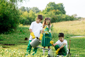 Two teenage boys and a girl of 8 years old in green clothes plant a tree in the garden