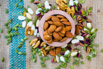 Sliced blanched almonds in wooden bowl & mixed nuts on a brown texture textile slate surface