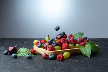 Summer berries in wooden plate:strawberries,cherries,raspberries,goosberry and blueberry,with fresh mint leaves.Copy space.