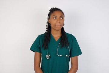 Photo of amazed puzzled young caucasian doctor female curves lips and has worried look, sees something awful in front, isolated on white background, wearing medical uniform.