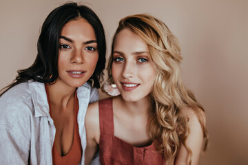 Dark-eyed adorable woman posing with blonde sister. Studio shot of pleasant caucasian ladies.