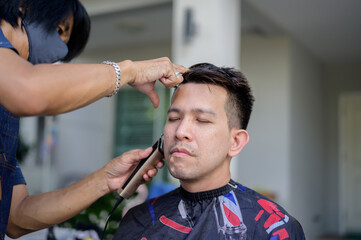 Asian man making haircut and salon business at home. Outdoor barbershop in garden. Social...