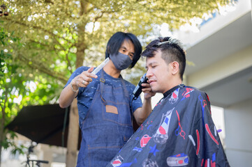 Asian man making haircut and salon business at home. Outdoor barbershop in garden. Social...