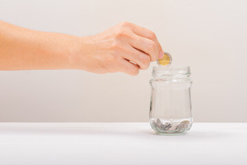 White hand man holding coin to putting in Jar or glass bottle for saving with soft white background. Saving money, Saving concept