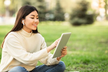 Female student using tablet, sitting in the park