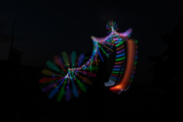 Long exposure shot, following the light trail from electrical juggling clubs that glow in changing colors, with the Juggler’s silhouette hidden between them.