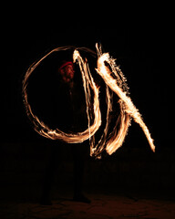 Long exposure shot from a fire juggling act, performed by a man with a red hat, showing the light trail create by the 3 burning torches. 