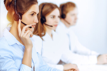 Call center operators. Focus on beautiful business woman using headset in sunny office