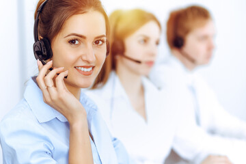 Call center operators. Focus on beautiful business woman using headset in sunny office