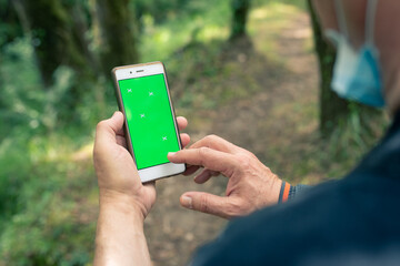 Senior man with facemask using smartphone in the forest