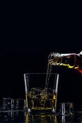 Whiskey pours from a bottle into a glass on a dark background