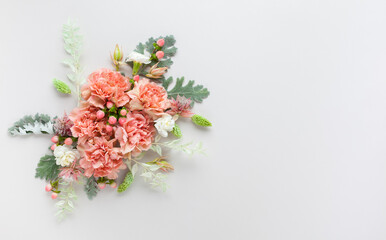 Obraz na płótnie Canvas Flowers composition made of coral carnation and silver-green leaves of Senecio cineraria on pastel grey background. Nature concept, copy space, flat lay.