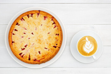 Homemade plum pie and cup of coffee cappuccino on white wooden tadle. Top view.