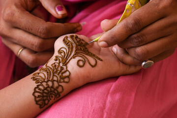 Woman applying beautiful henna, Mehndi tattoo Arabic design on young Indian girls hands at City...