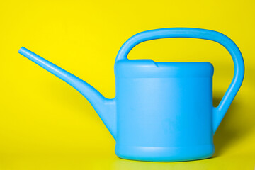 Blue watering can on a yellow background. The watering can has a place for an inscription or logo. Gardening concept