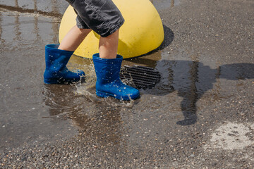 Children in the summer after the rain. Close-up of a boy's feet in blue rubber boots jumping in puddles on a walk. Children have fun playing outdoors in rainy weather. Waterproof boots for boys. в рез