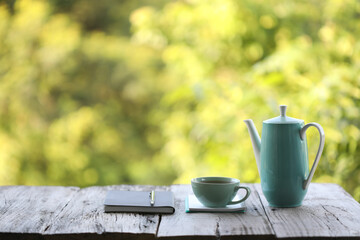Teal teapot and cup with black book on rustic wooden  table with green leaves background