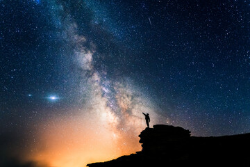 Person pointing the Milky Way with his hand. Small human silhouette contemplating the immensity of...