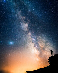 Man and the Universe. A person is standing on the top of the hill and pointing the Milky Way with...