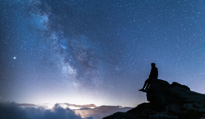 Person sitting on a rock contemplating the vastness of the universe. Silhouette of a man under the...
