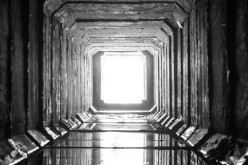 Square concrete drainage tunnel with light in the end.