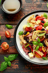 Antipasto salad with pasta, tomato, olives, red onion, bell pepper, salami, cheese, artichoke and basil.