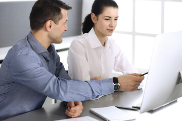 Cheerful smiling businessman and woman working with computer in modern office. Headshot at meeting or workplace. Teamwork, partnership and business concept