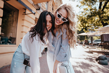 Laughing enthusiastic girls walking down the street. Refined female friends smiling during weekend rest.