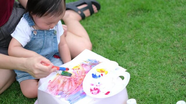 Funny little girl with painted . Learning and education of kid at garden outdoor.Happy family mother and daughter together paint. Asian woman helps her child girl.