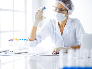 Professional female scientist in protective eyeglasses researching tube with reagents in laboratory. Concepts of medicine and science researching