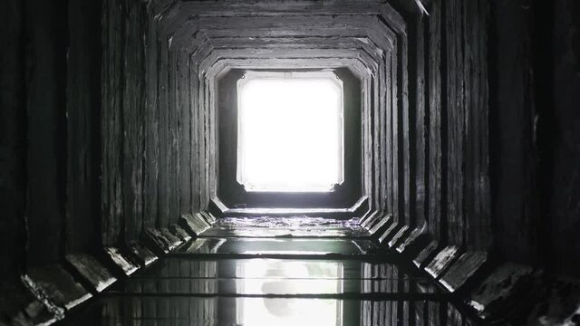 Square concrete drainage tunnel with light in the end, timelapse.