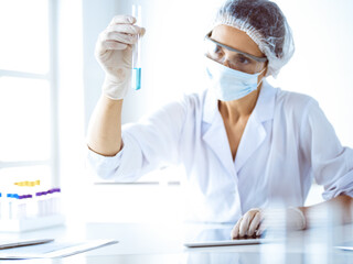 Professional female scientist in protective eyeglasses researching tube with reagents in laboratory. Concepts of medicine and science researching