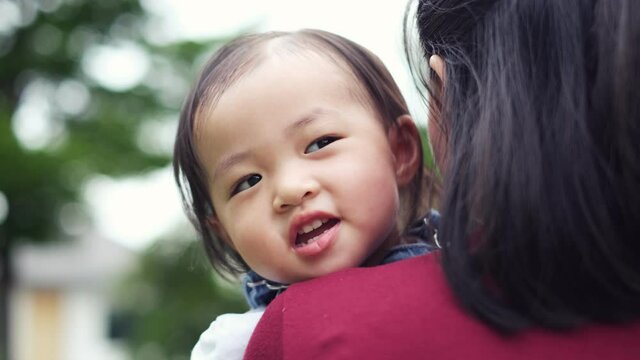 Slow motion of 1 year old cute toddler Asian boy kid in bib jeans holding mother hand and walking together..Asian mother holding hand of little  with backpack outdoors, 