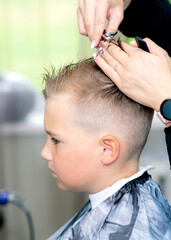 Serious school boy ready getting trendy haircut from expirienced barber at fashionable hairdressing salon.