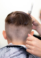 Close up rear view american pretty school boy trendy haircut at bright modern barbershop.
