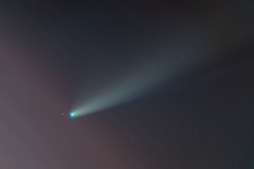 Comet C / 2020 F3 (NEOWISE) in the twilight sky among the clouds. Photo of a real comet through a telescope. Long blurry comet tail. A bright green comet surrounded by a nebula.