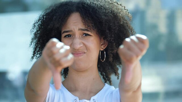 Young beautiful African American woman holds out hands, gives thumbs down gesture of frustration and disgust. Girl expresses her true negative emotions, looks disapprovingly, shakes her head, said No.