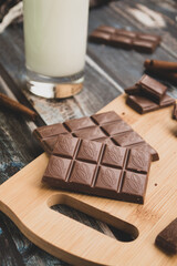 milk dark chocolate tiles on wood cutting board, wooden background