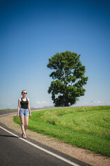 Young woman walking along the road. Traveling alone. Hitchhiking without luggage. Isolation.