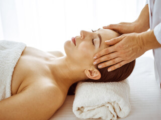 Beautiful brunette woman enjoying facial massage with closed eyes. Relaxing treatment in medicine and spa center concepts