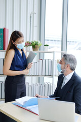 Senior Caucasian boss and young businesswoman wearing mask preventing for Covid 19 virus holding document sheet and talking about job in office. Social distance and new normal lifestyle concept