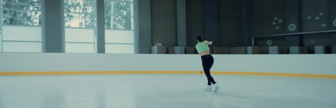 Professional teenager female ice figure skater practicing jumps on the rink. Shot on RED cinema camera with 2x Anamorphic lens, 75 FPS slow motion