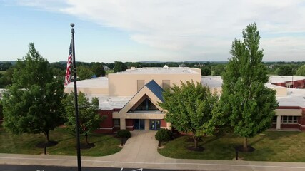 Public school in America with American flag above bus zone parking, education theme, closed for COVID no students,, aerial push-in shot