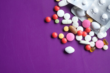 close up of colorful pills spilling on purple background 